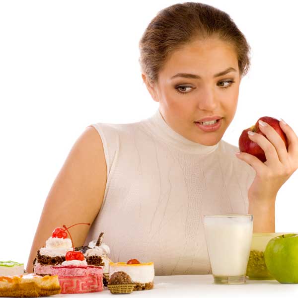 A woman holds an apple but is staring at cake.