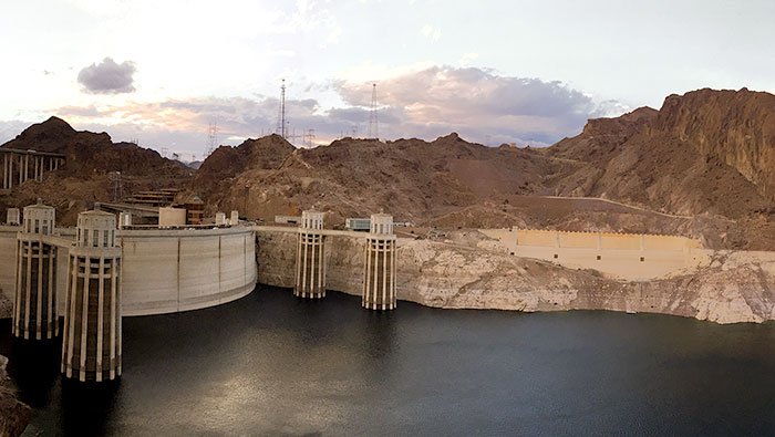 Reservoir-side photo of a lake and dam showing light colored rock where the water used to be.